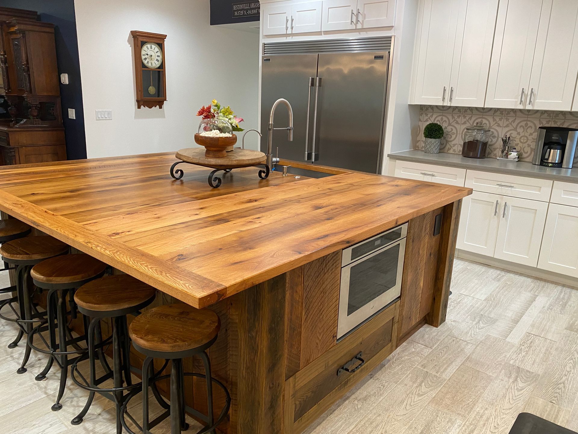 Rustic kitchen island with wooden countertop, stools, built-in microwave, and stainless steel refrigerator.