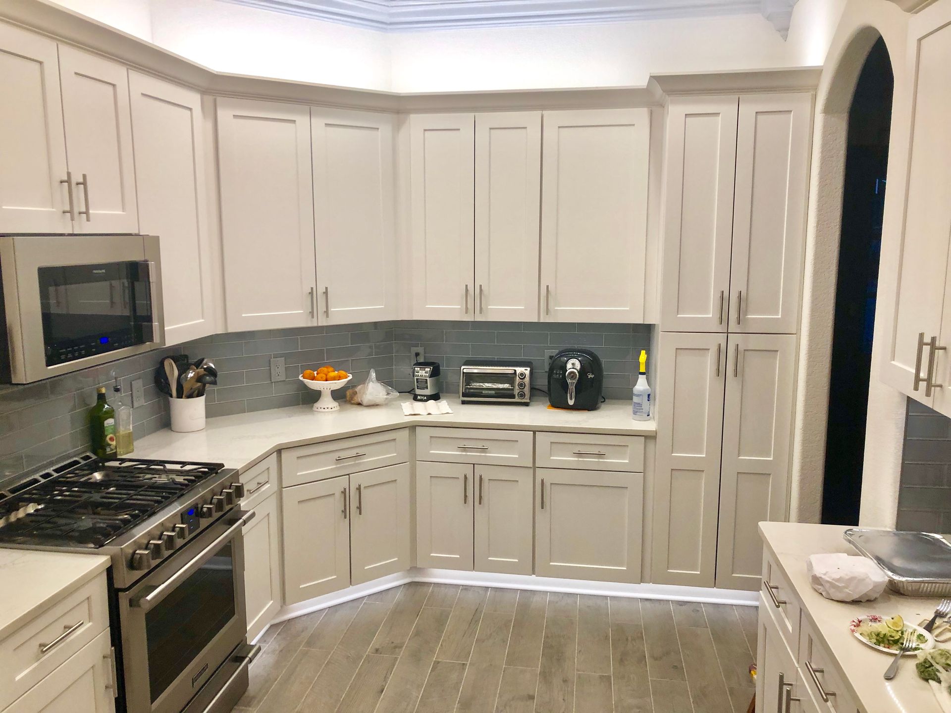 White kitchen with stainless steel appliances, light wood floor, and light blue backsplash.