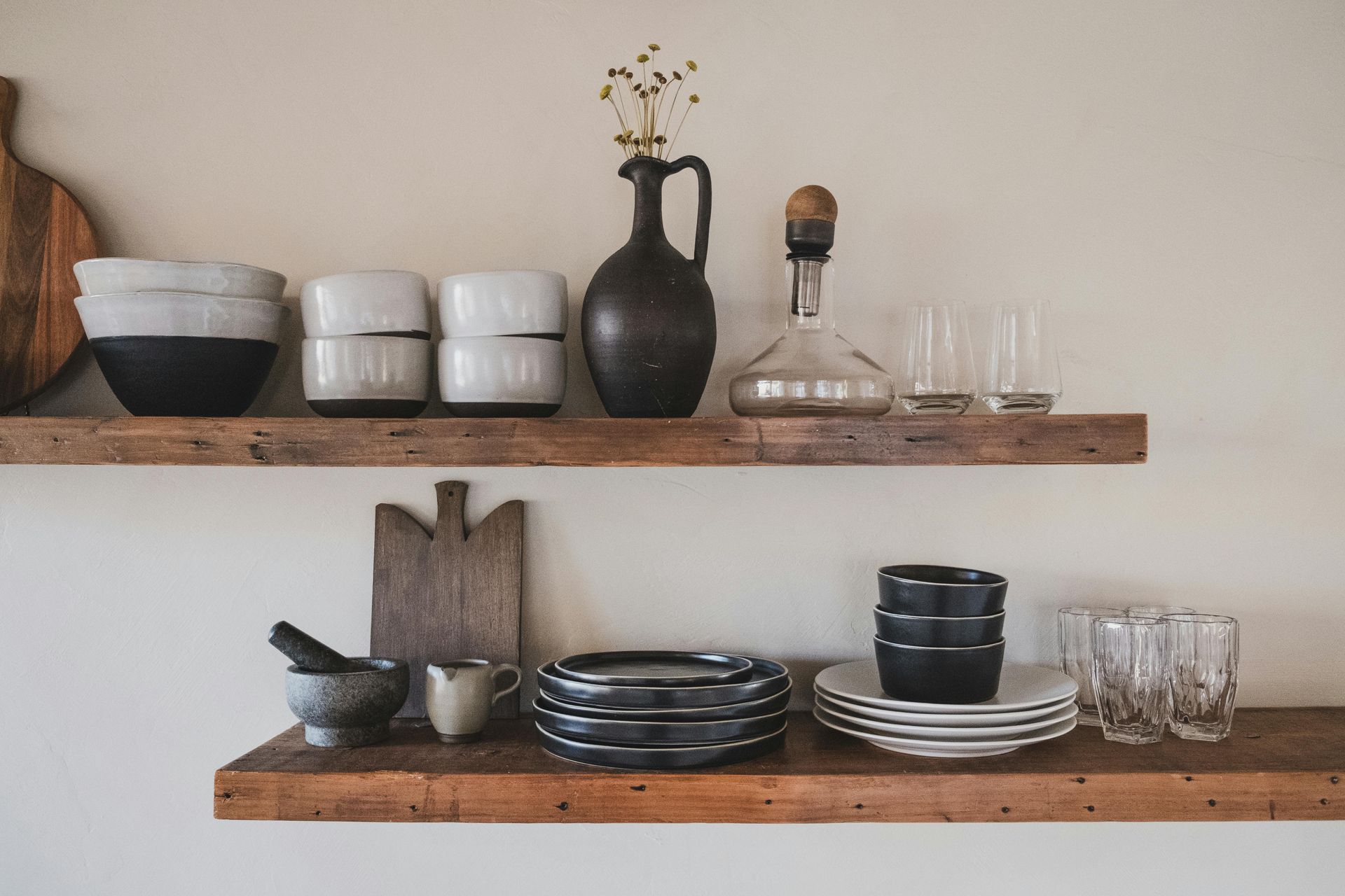 Wooden shelves with pottery, glassware, and kitchen items on a cream-colored wall.