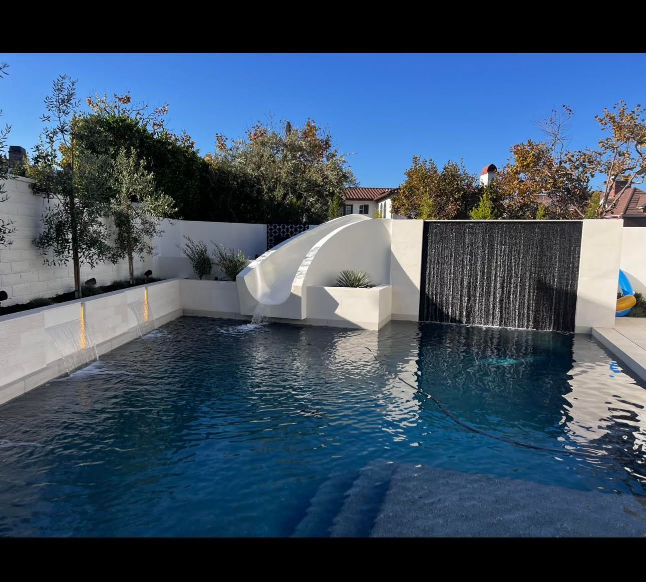 Pool with slide and waterfall against a blue sky.
