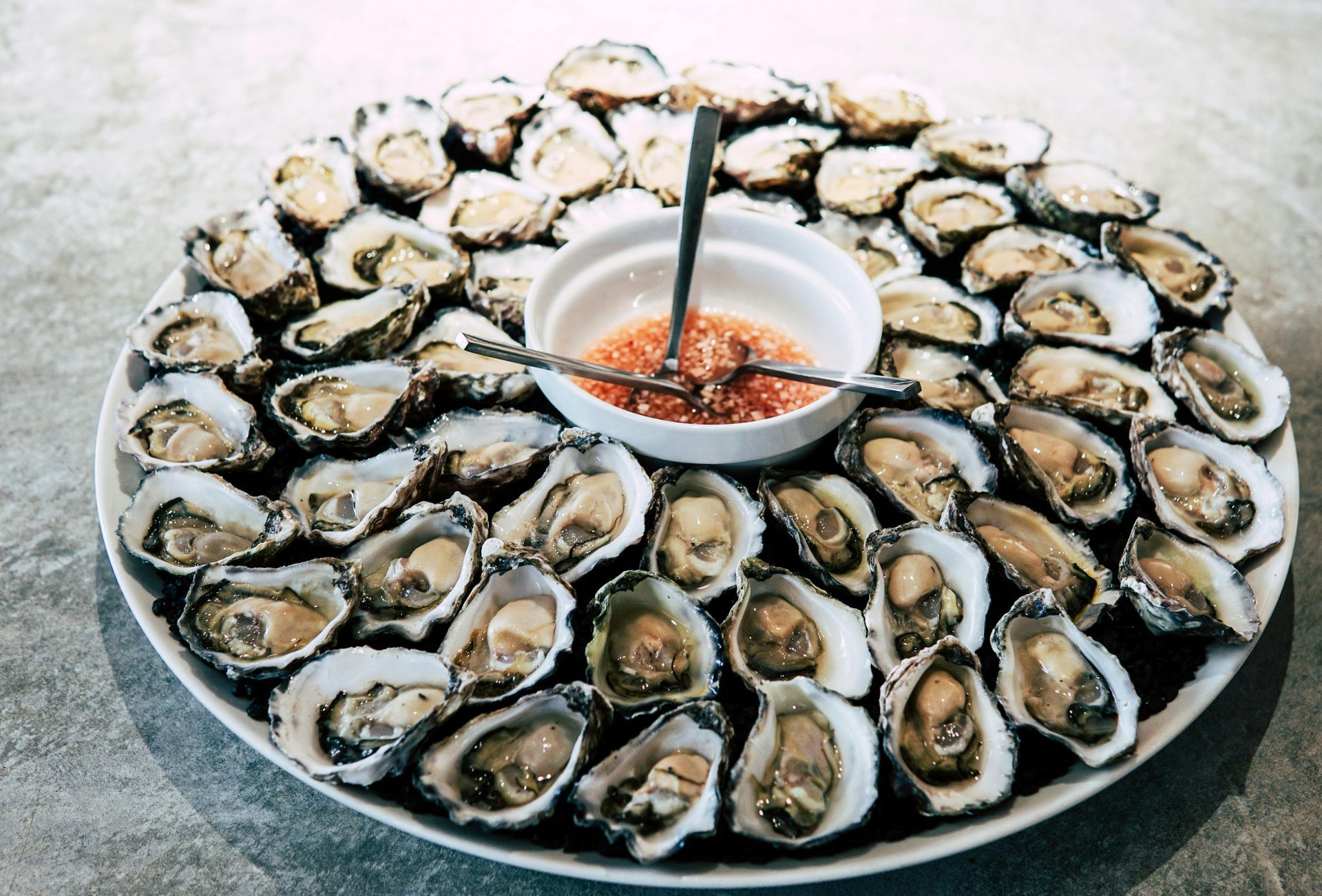 A plate of oysters with sauce and a spoon