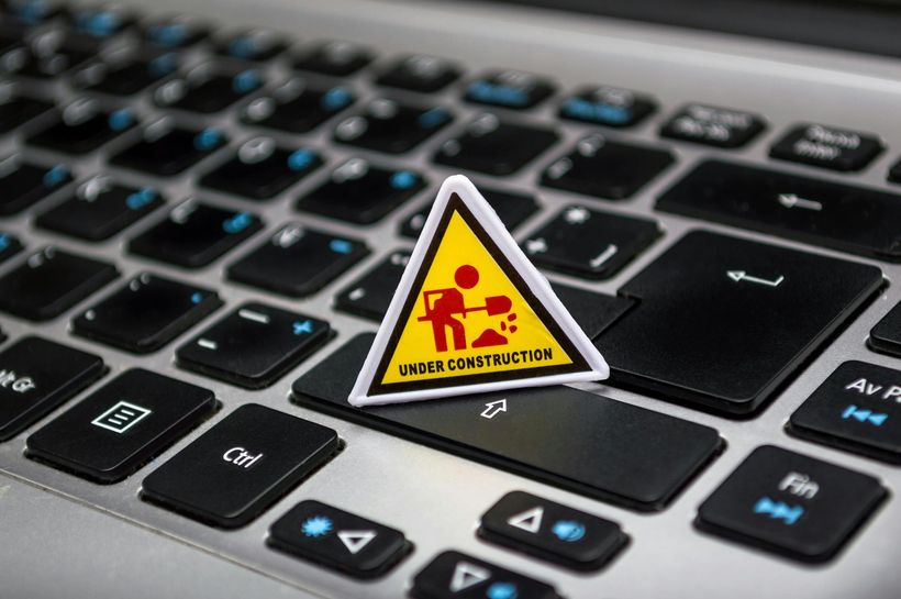 A yellow under construction sign is sitting on top of a laptop keyboard.