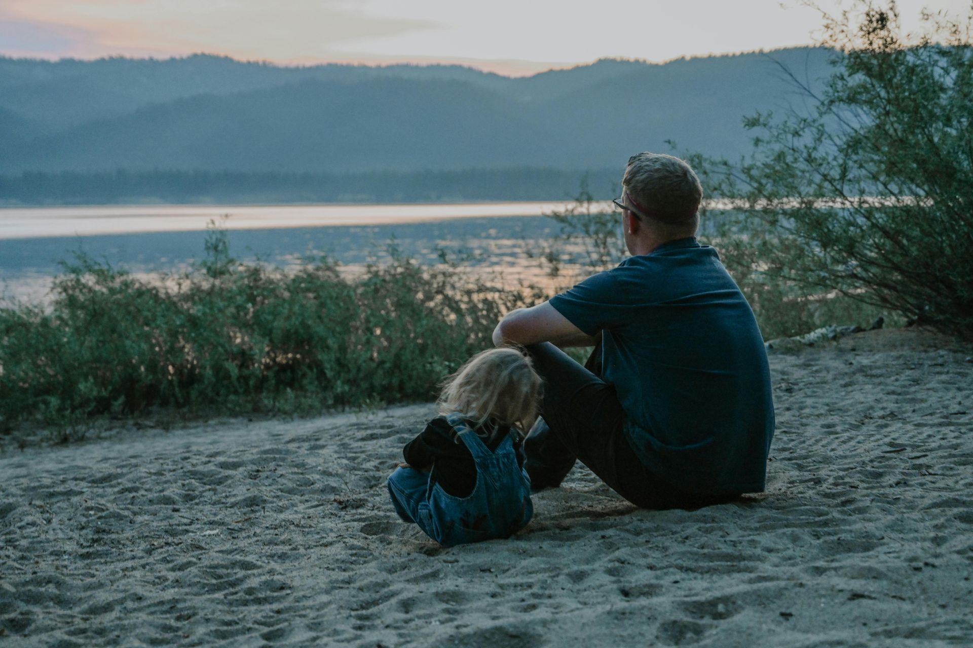 A man and a child are sitting on the beach looking at the water.