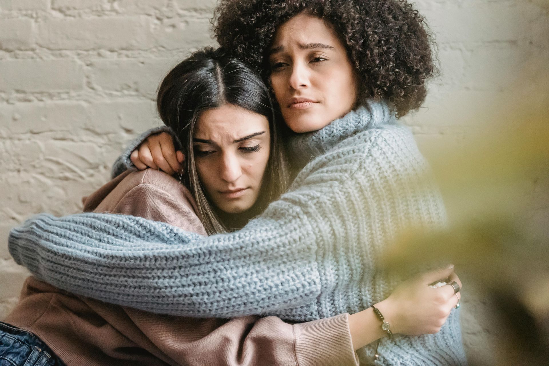 Two women are hugging each other in front of a brick wall.