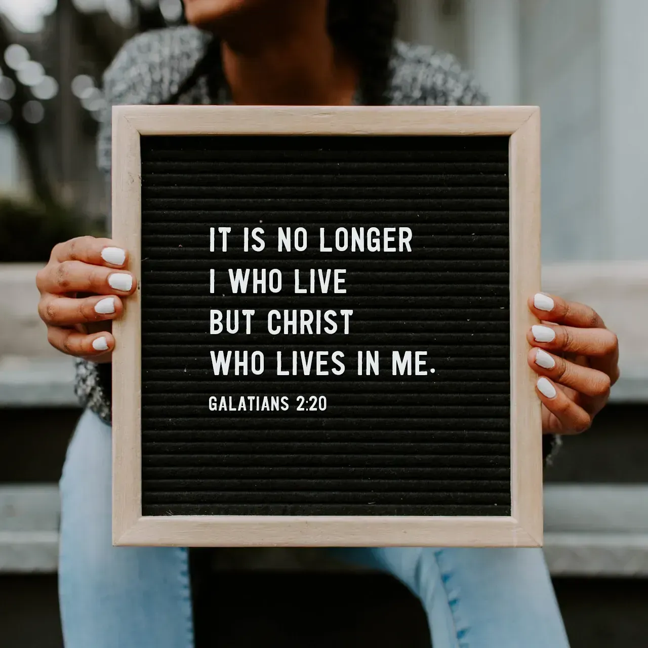 A woman is holding a sign that says it is no longer i who live but christ who lives in me.