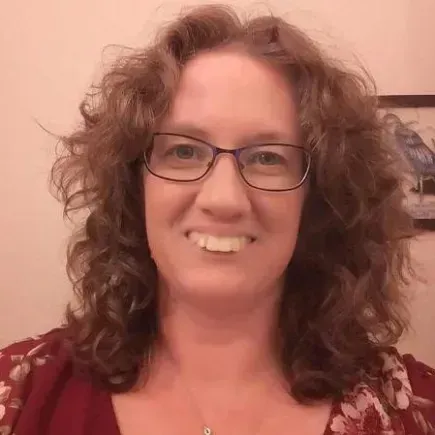 A woman with curly hair and glasses is smiling for the camera.