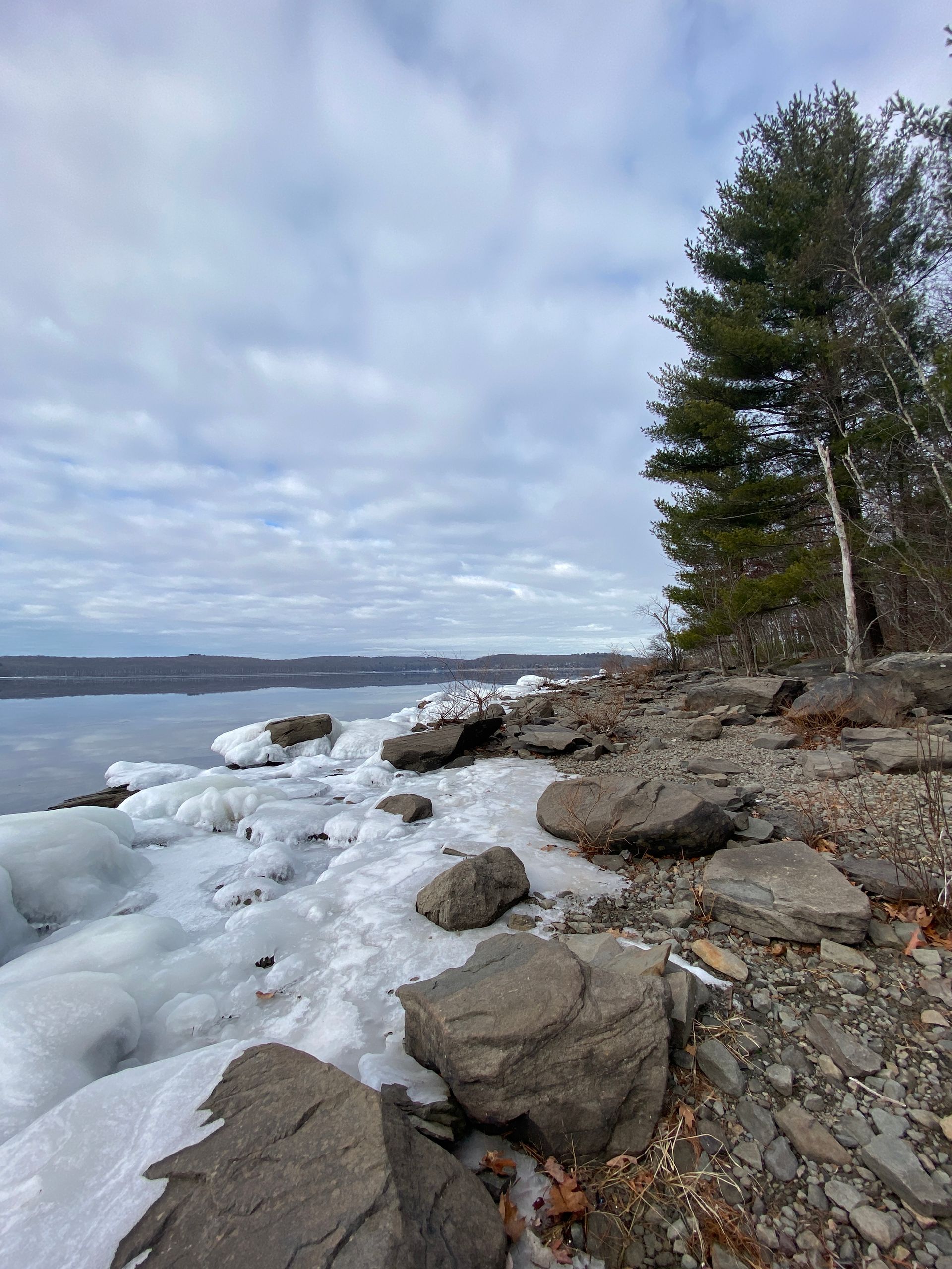 A rocky shoreline covered in snow and ice with a lake in the background.