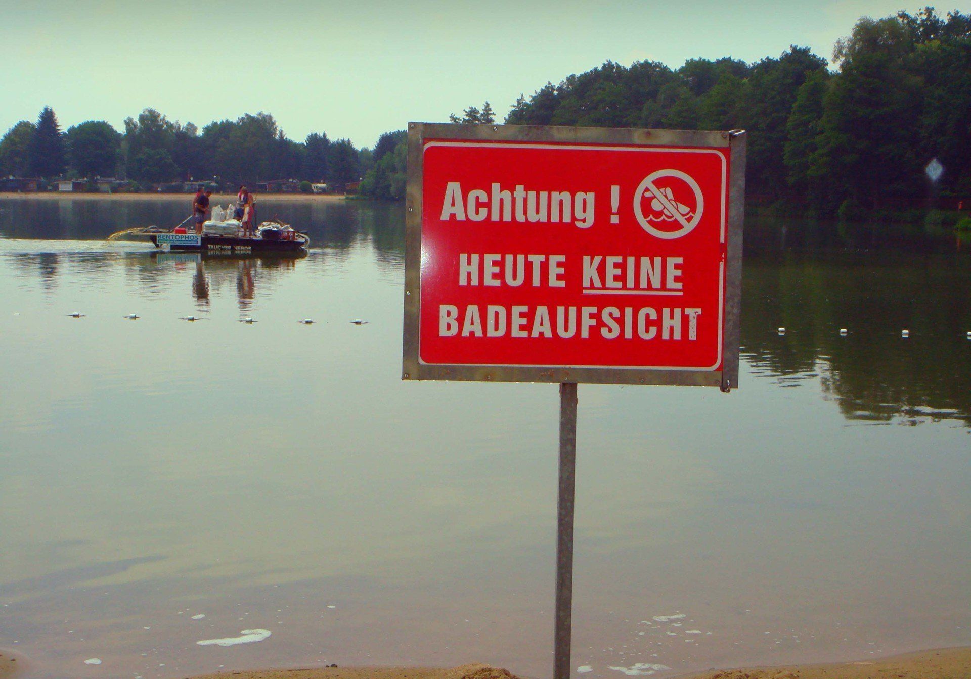 A red sign that says achtung in front of a body of water