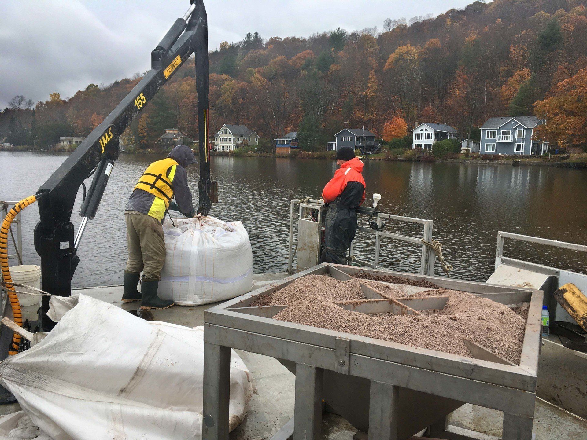 Two men are loading a large bag of sand onto a boat.