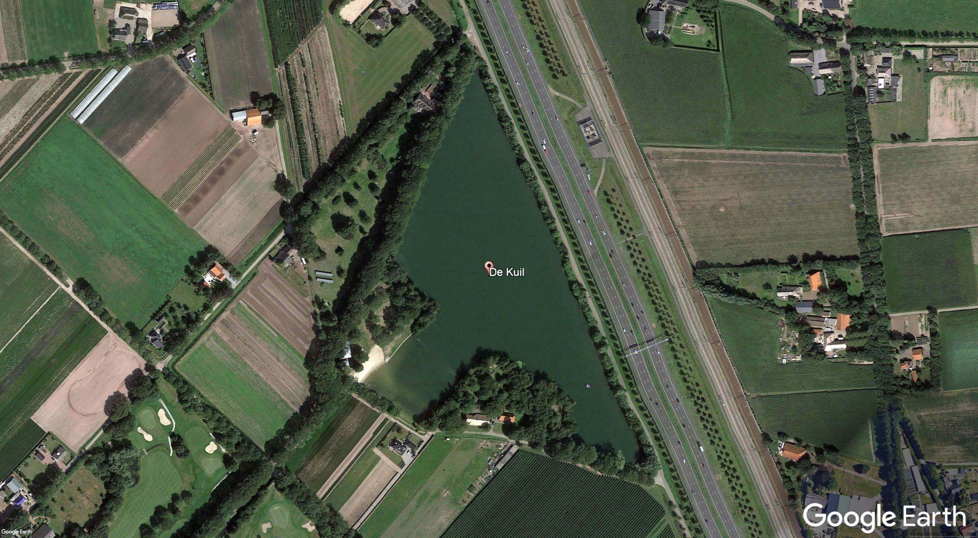 An aerial view of a lake surrounded by fields and a highway