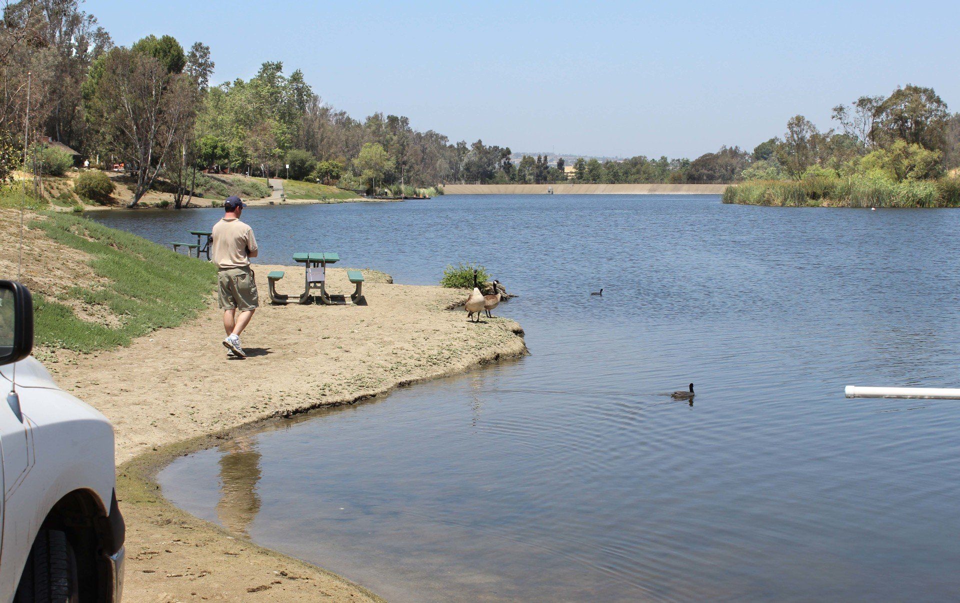 A man is fishing in a lake near a picnic table