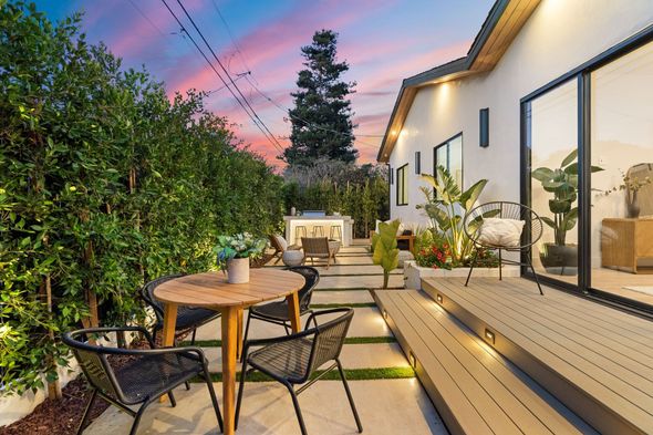 Patio moderne dans le jardin avec table ronde, chaises, terrasse en bois, plantes en pot et ciel au coucher du soleil