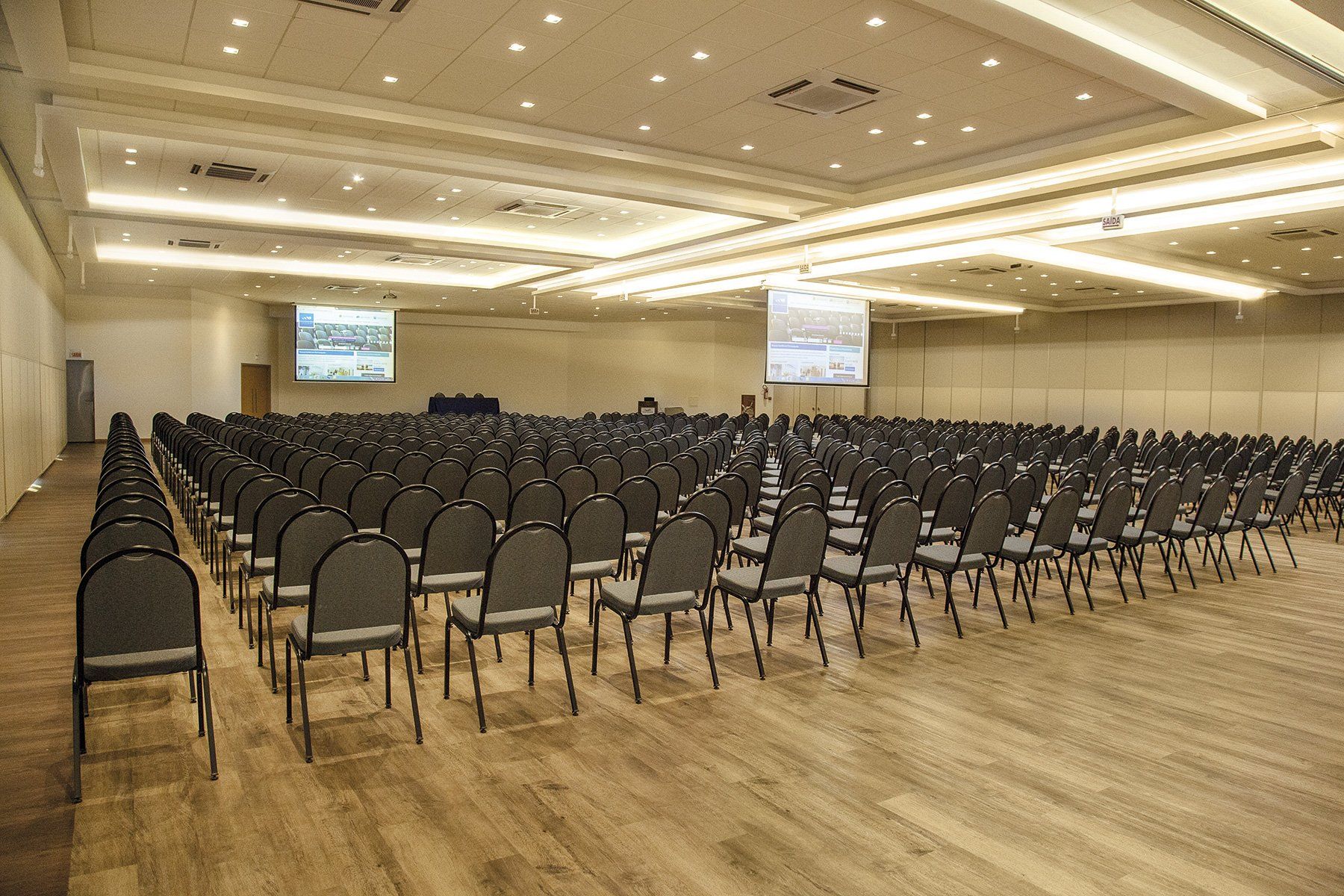 Uma grande sala de conferências com fileiras de cadeiras e uma tela de projeção.