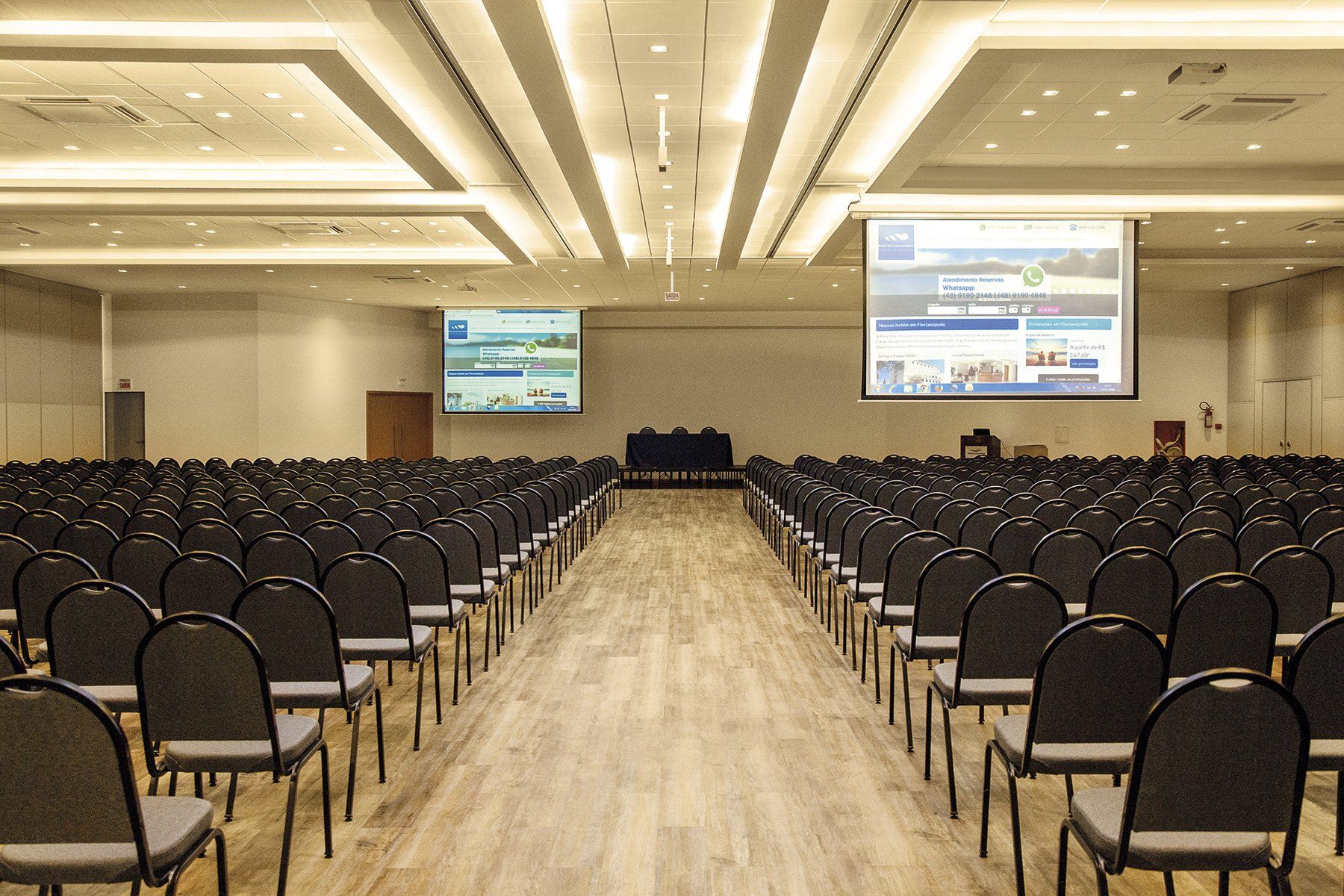 Uma grande sala de conferências com fileiras de cadeiras e uma tela de projeção