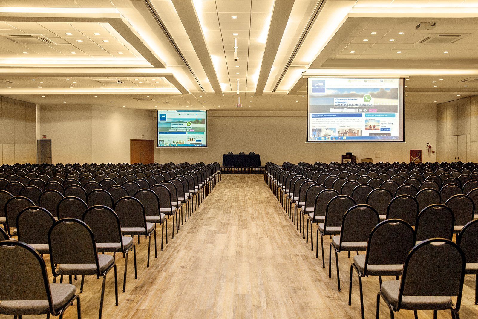 Uma grande sala de conferências com fileiras de cadeiras e uma tela de projeção.