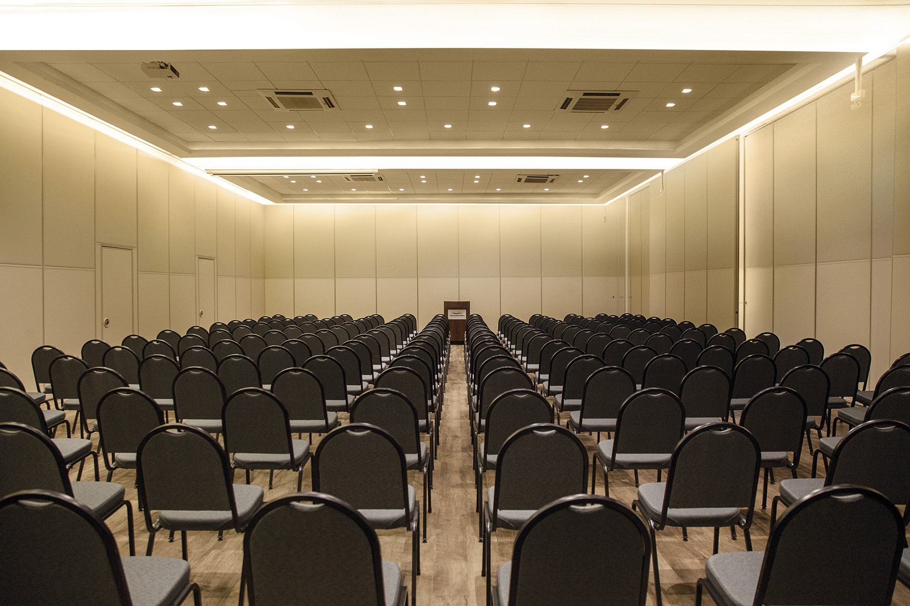 Fileiras de cadeiras pretas estão alinhadas em uma grande sala.