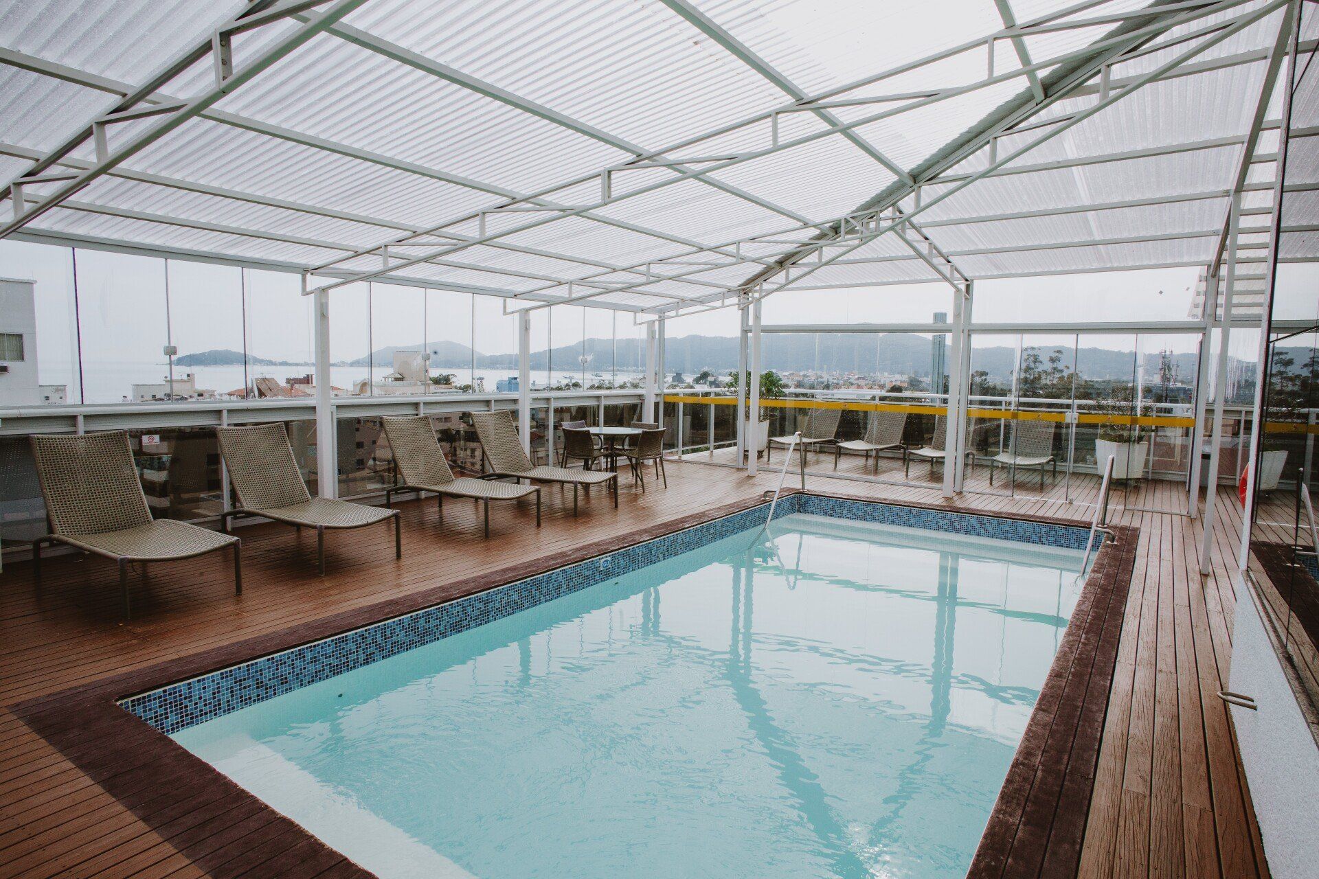 Uma grande piscina com teto transparente e cadeiras ao redor.