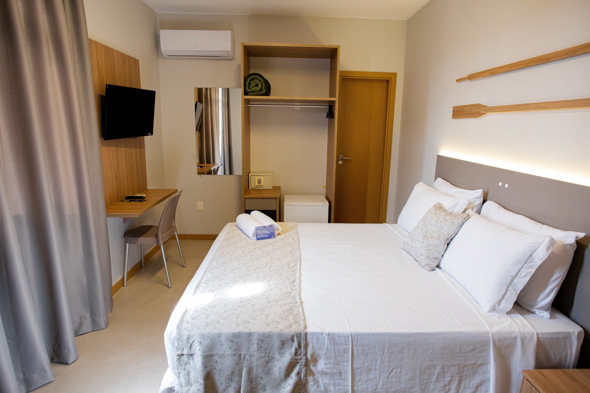 Um quarto de hotel com cama, mesa, televisão e espelho.