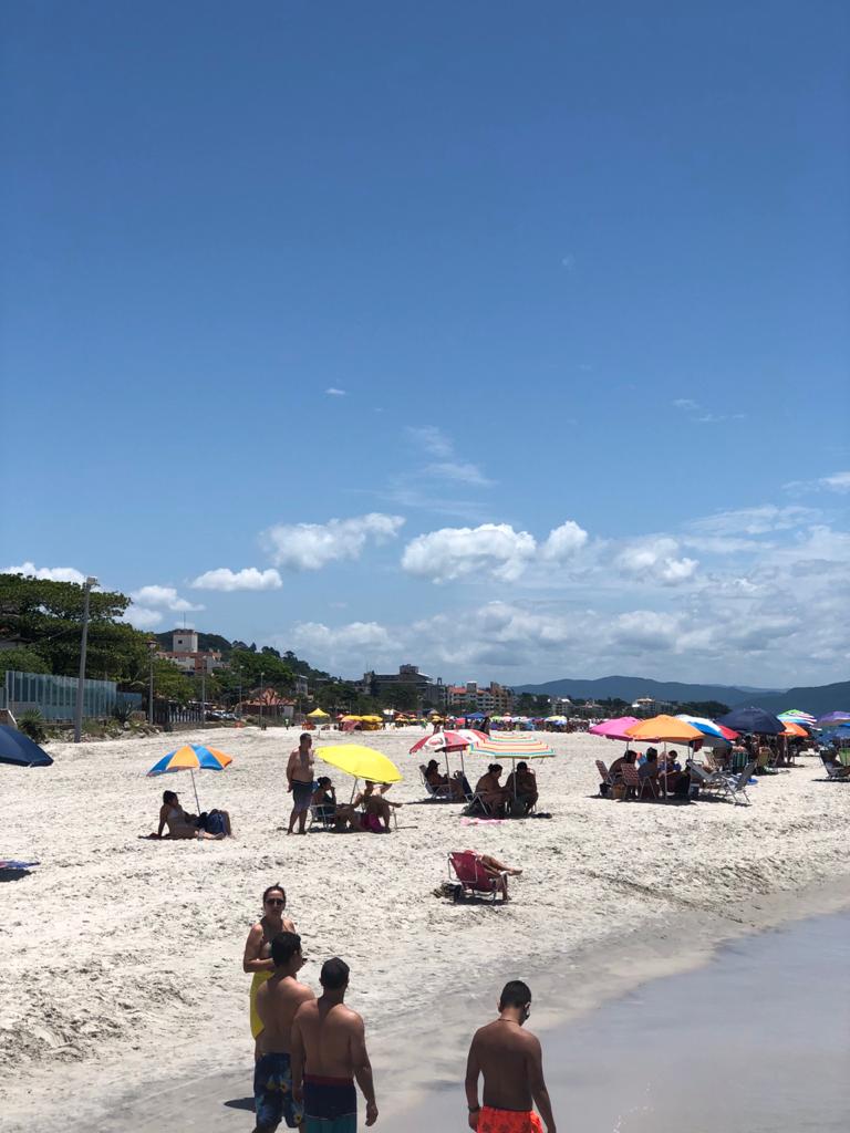 Uma praia cheia de gente e guarda-sóis em um dia ensolarado.