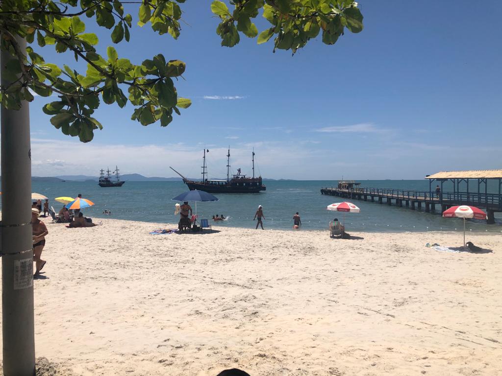 Uma praia com gente e guarda-sóis e um barco na água.