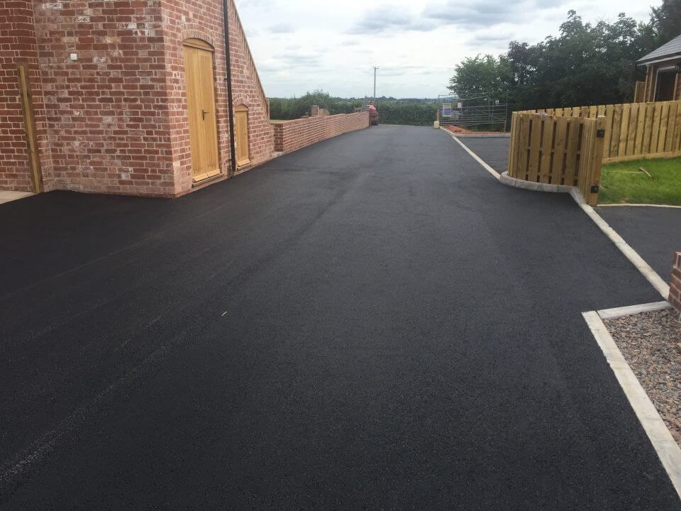 A black asphalt driveway with a brick building in the background