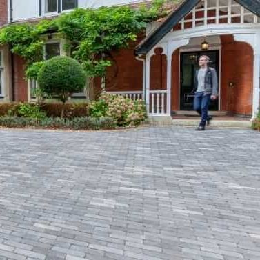 A man is walking down a brick driveway in front of a house.