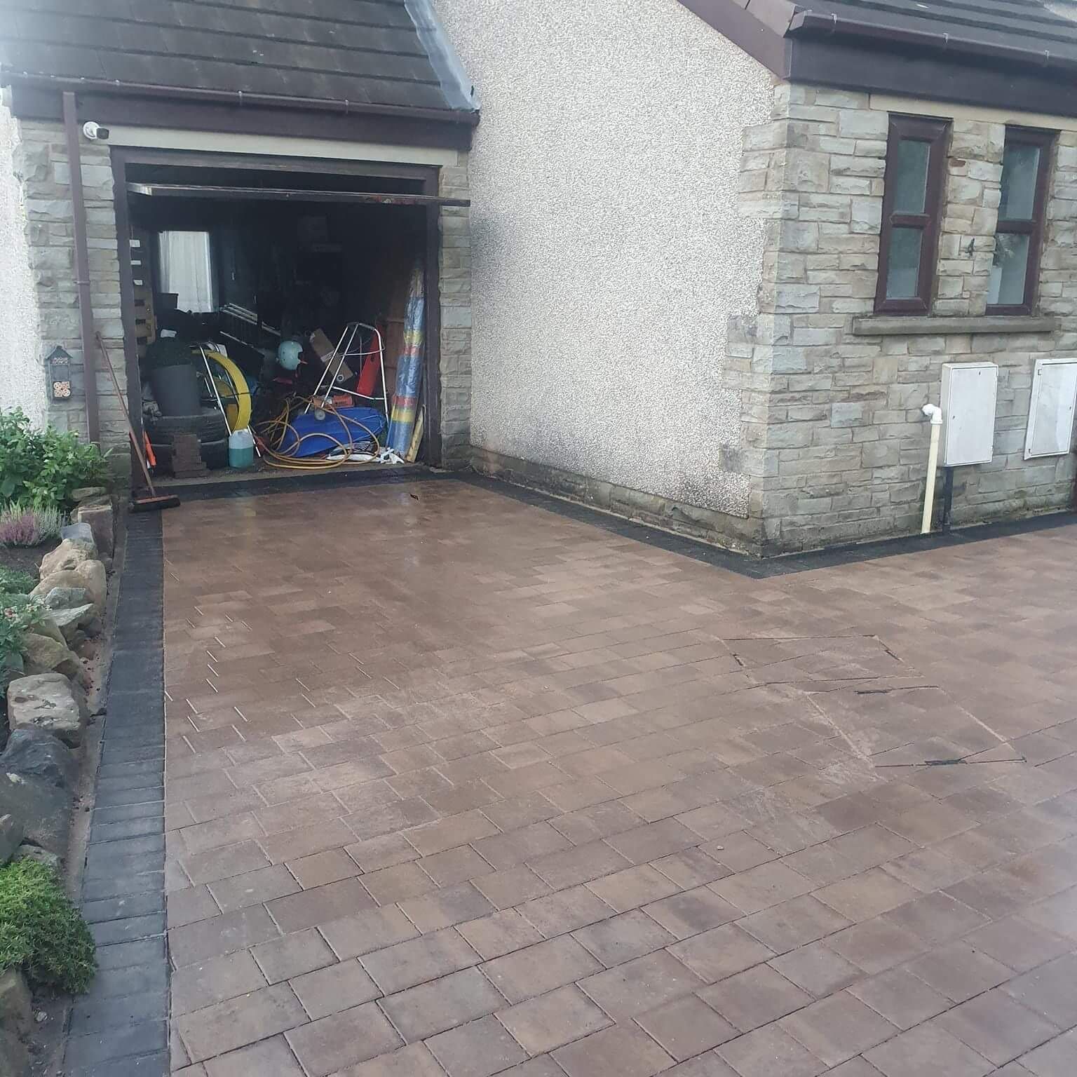 A brick driveway leading to a garage with a brick building in the background.