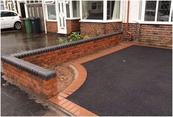 A driveway with a brick wall and a car parked in front of it.