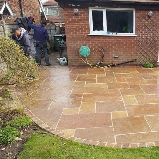 A group of people are working on a patio in front of a brick house.