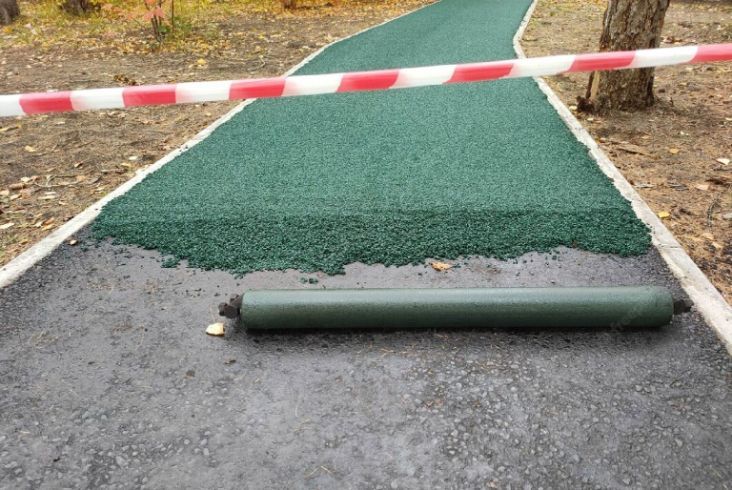 A roll of green rubber is laying on the ground next to a road.