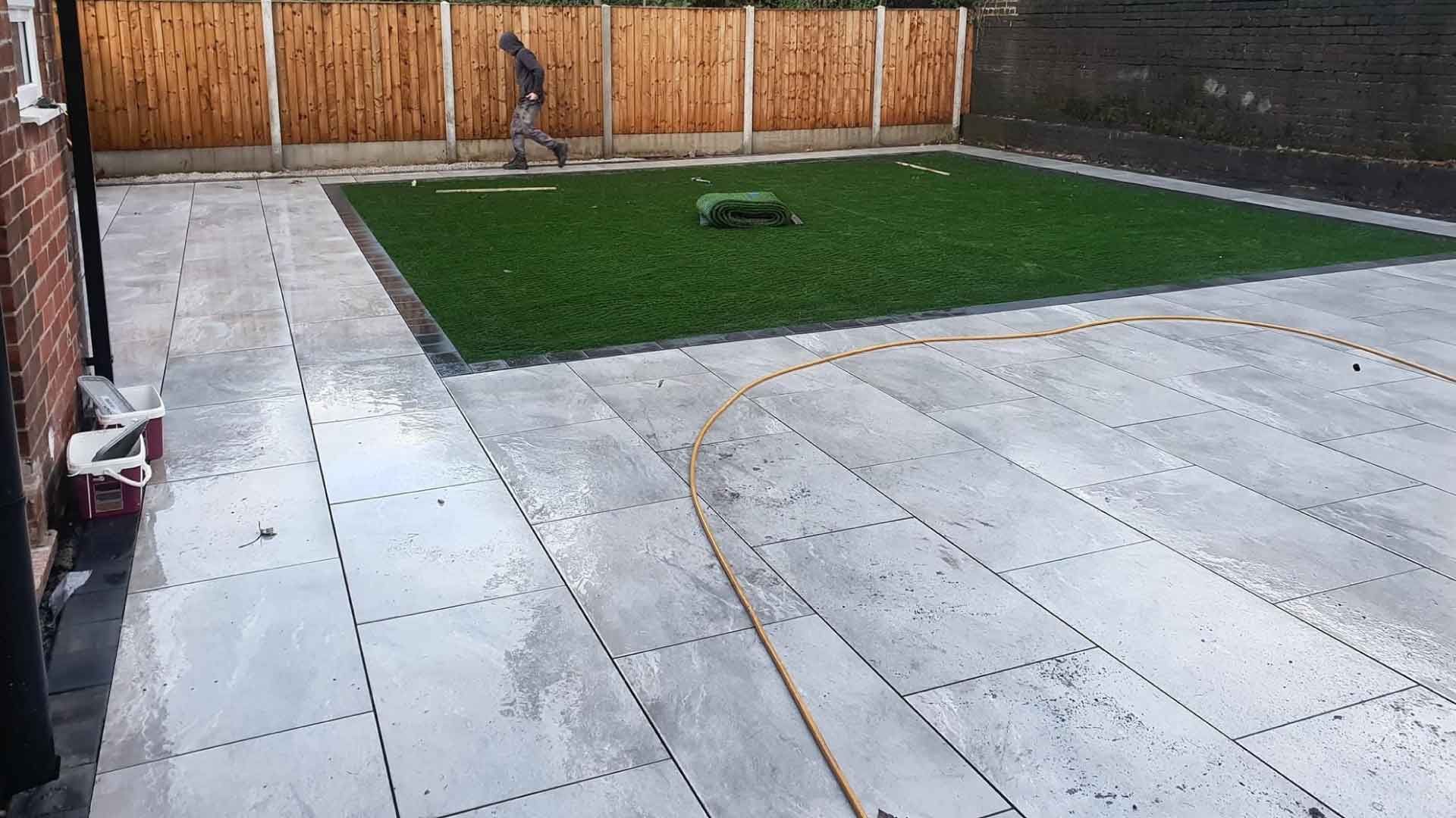 A man is standing in a backyard with a lawn and a fence.