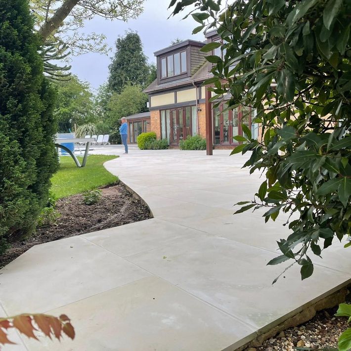 A concrete walkway leads to a large house surrounded by trees.