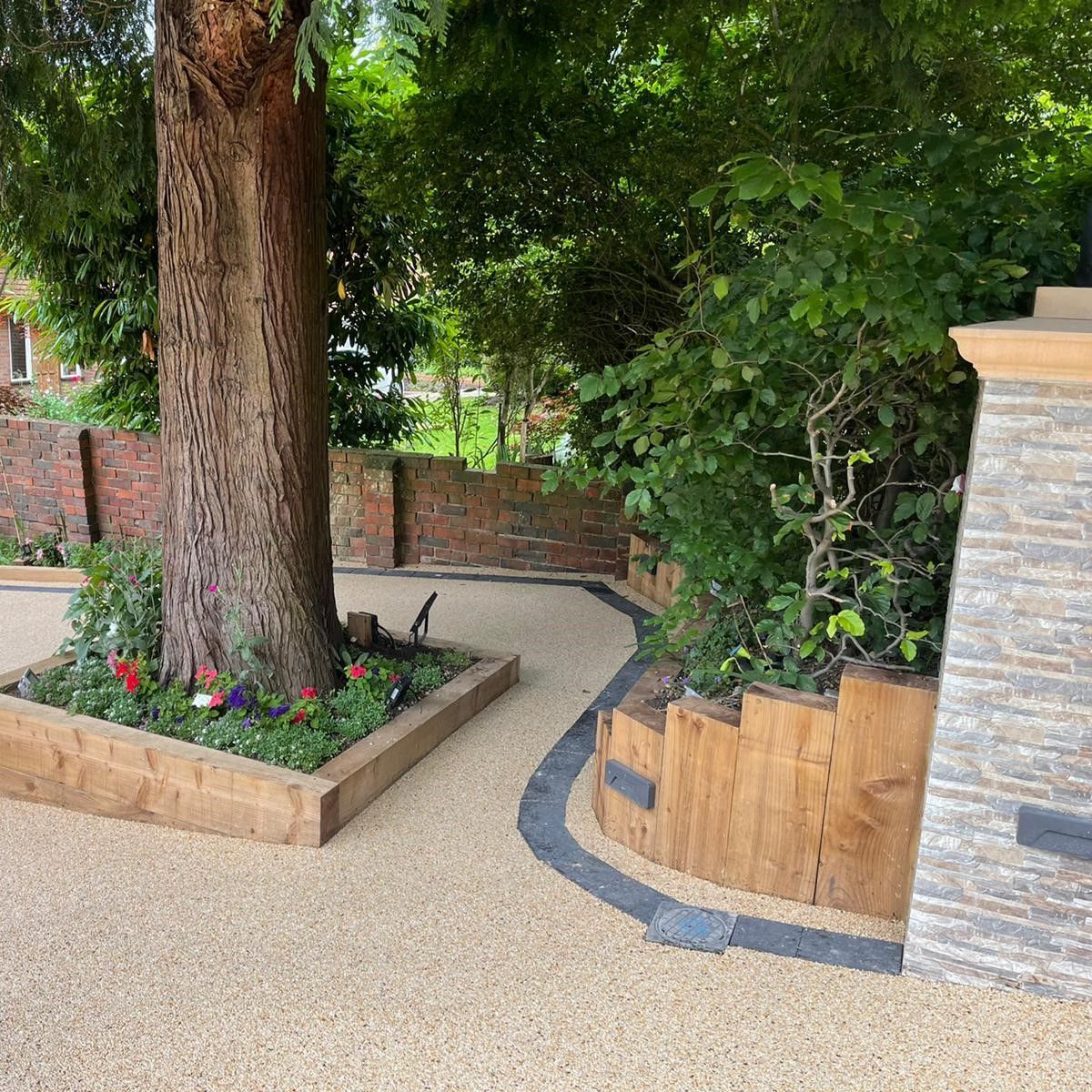 A tree is in the middle of a garden next to a stone wall.