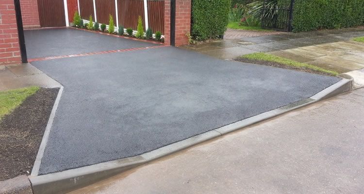 A black asphalt driveway with a brick fence in the background.