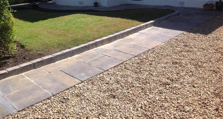 A gravel driveway with a sidewalk leading to a house.