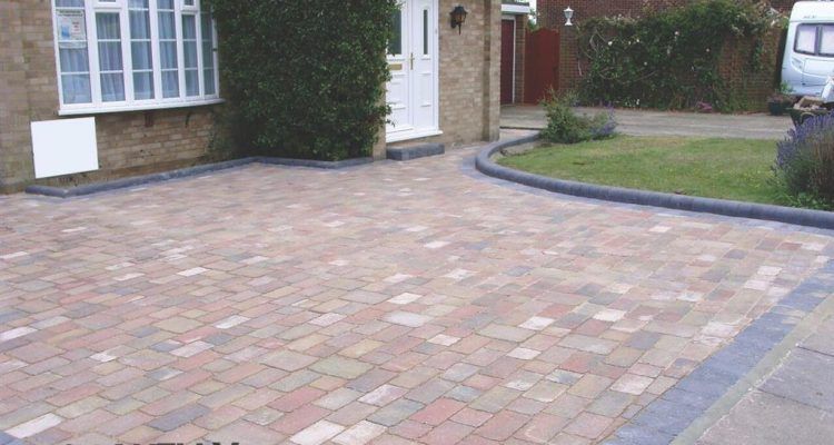 A brick driveway leading to a house with a white van parked in front of it.