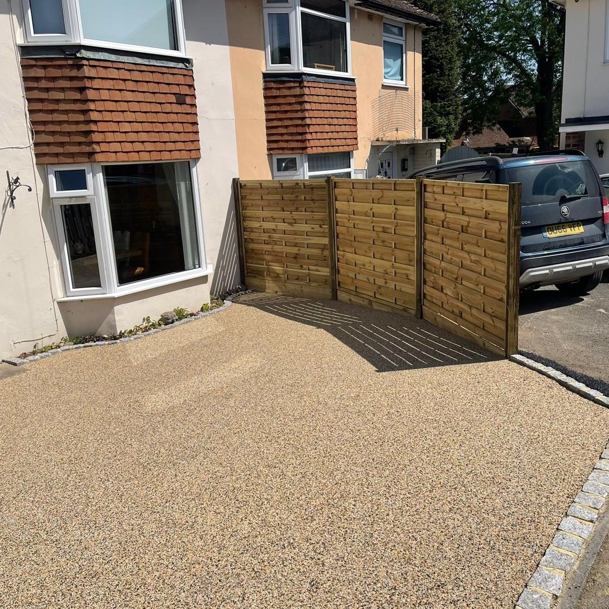 A car is parked in front of a house with a wooden fence.