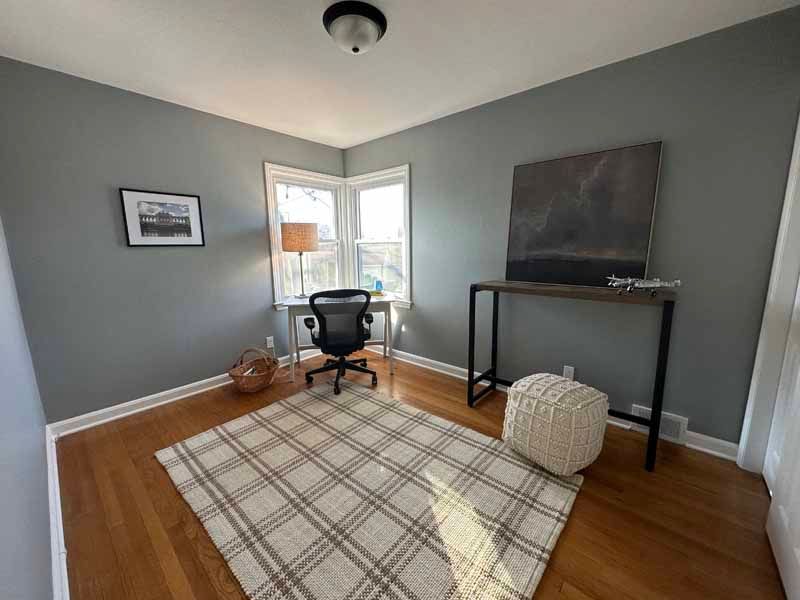 A room with a desk , chair , rug and painting on the wall.
