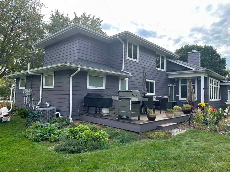 A large purple house with a deck and a grill in the backyard.