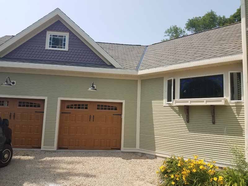 A car is parked in front of a house with three garage doors.