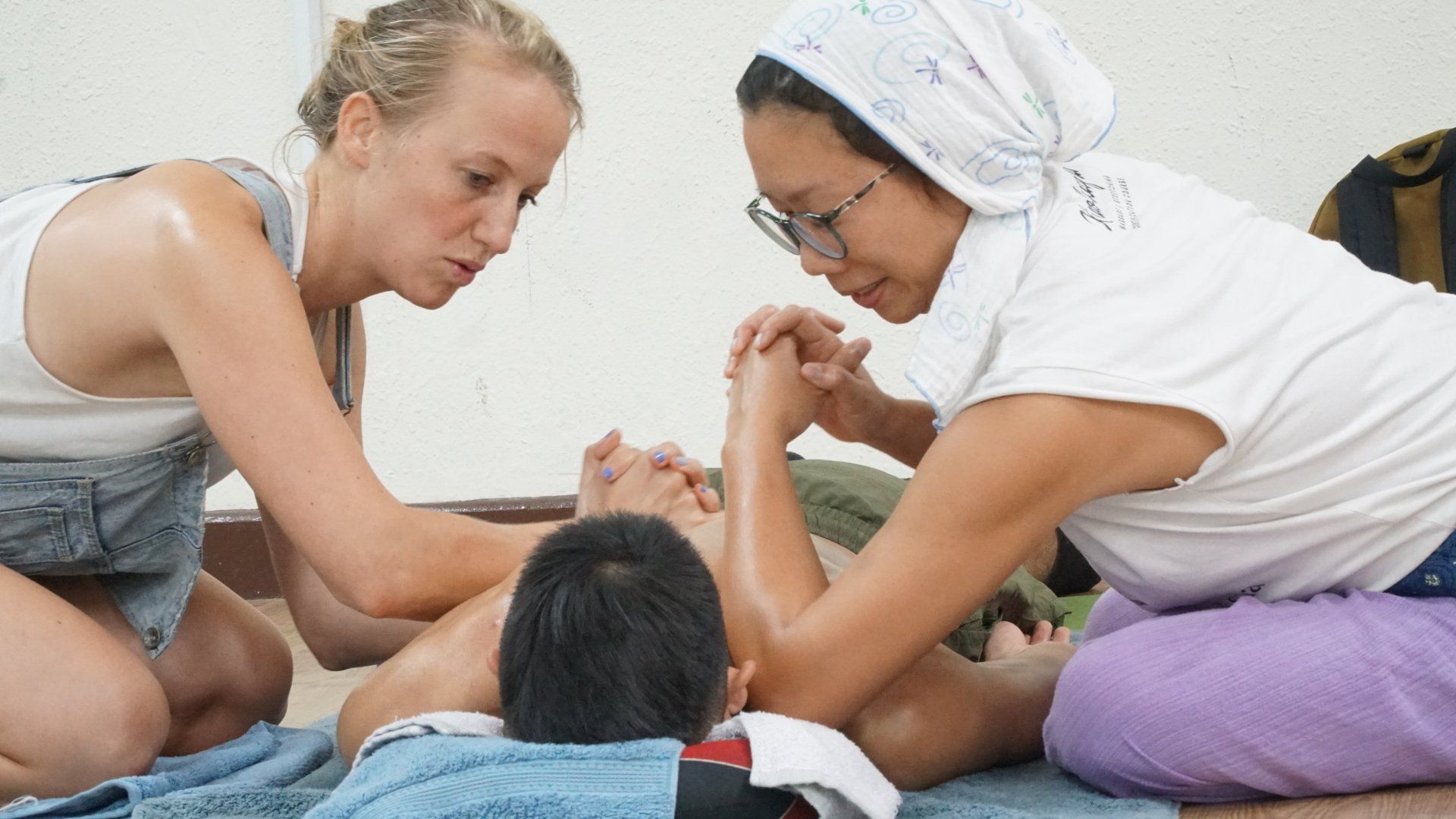 Two women are giving a child a massage on a blue towel