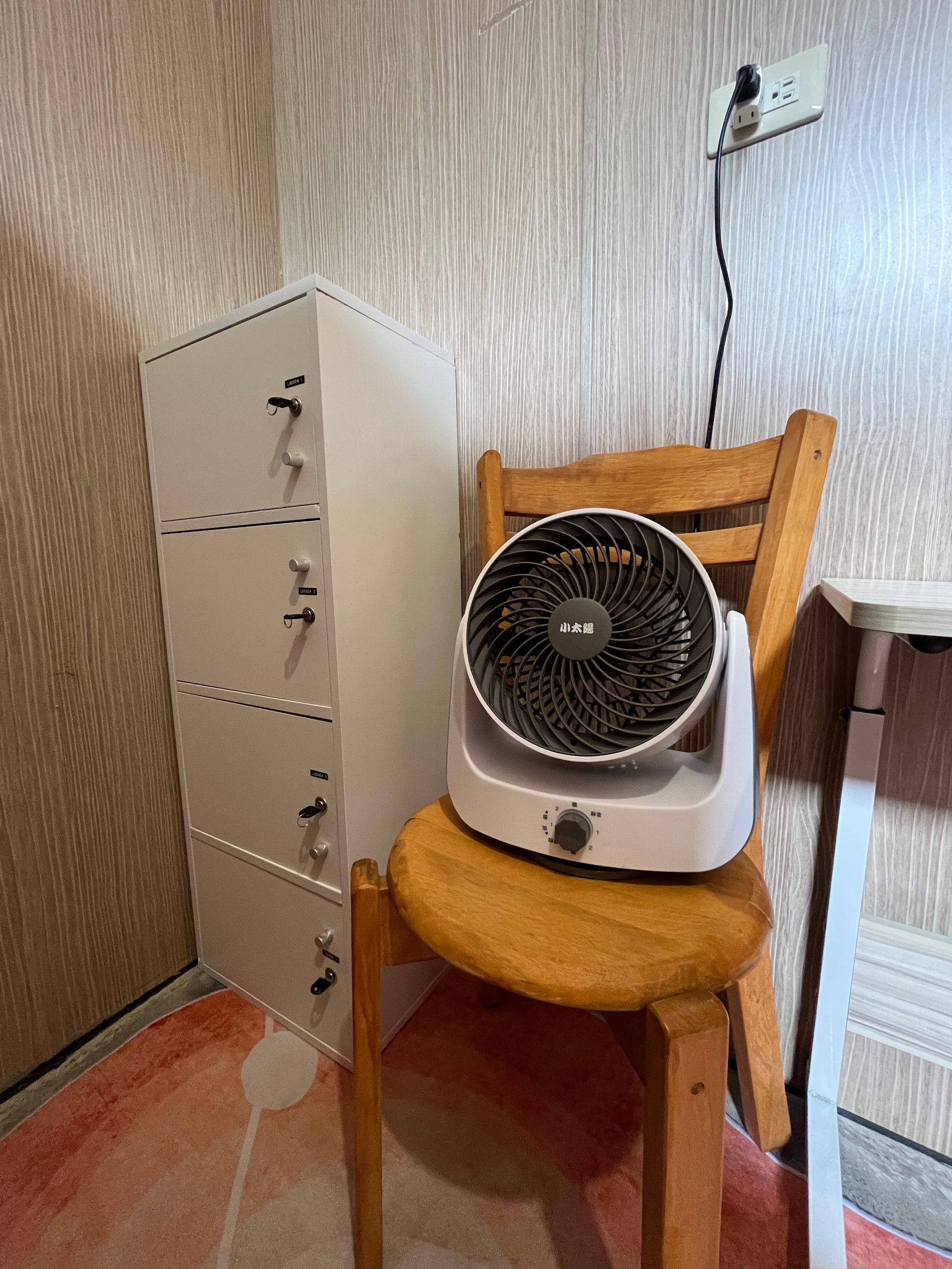 A fan is sitting on a wooden chair next to a dresser.