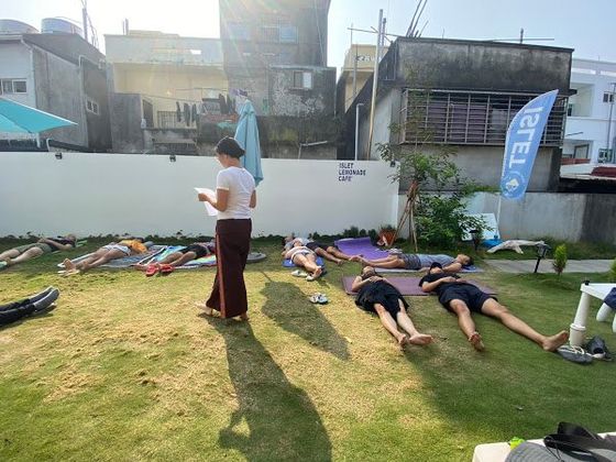 A group of people are laying on yoga mats on the grass.