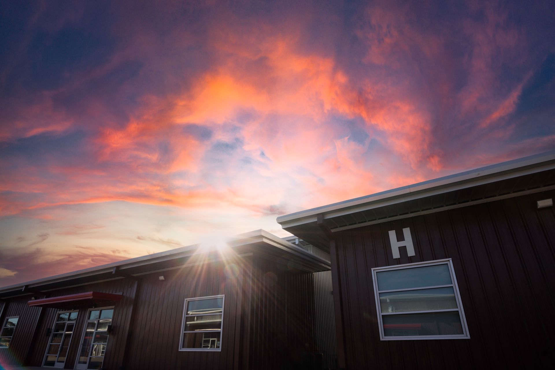 The sun is shining through the clouds over a building with the letter h on it.