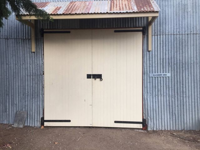 Large, cream-colored double doors with black hinges and handle, under a corrugated metal awning. 