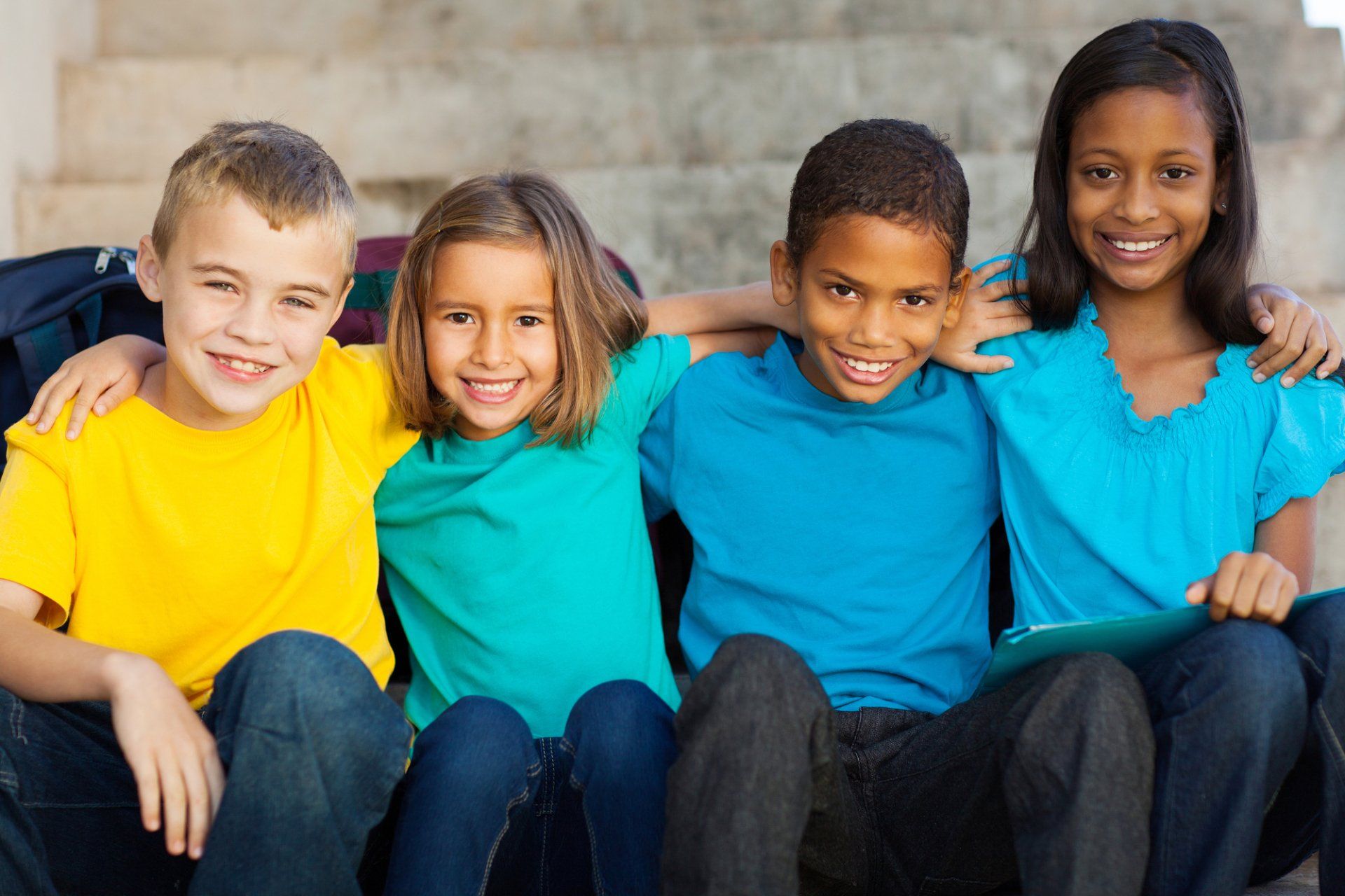 Four children with arms around each other, smiling, sitting on steps.