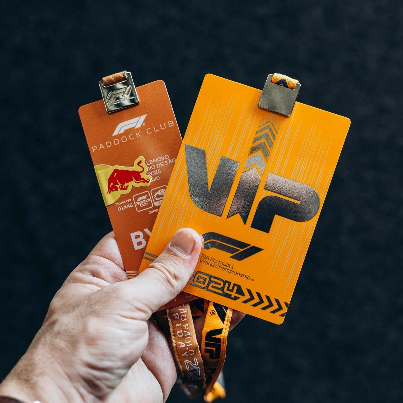 Hand holding two orange VIP passes for a Formula 1 race. One says 