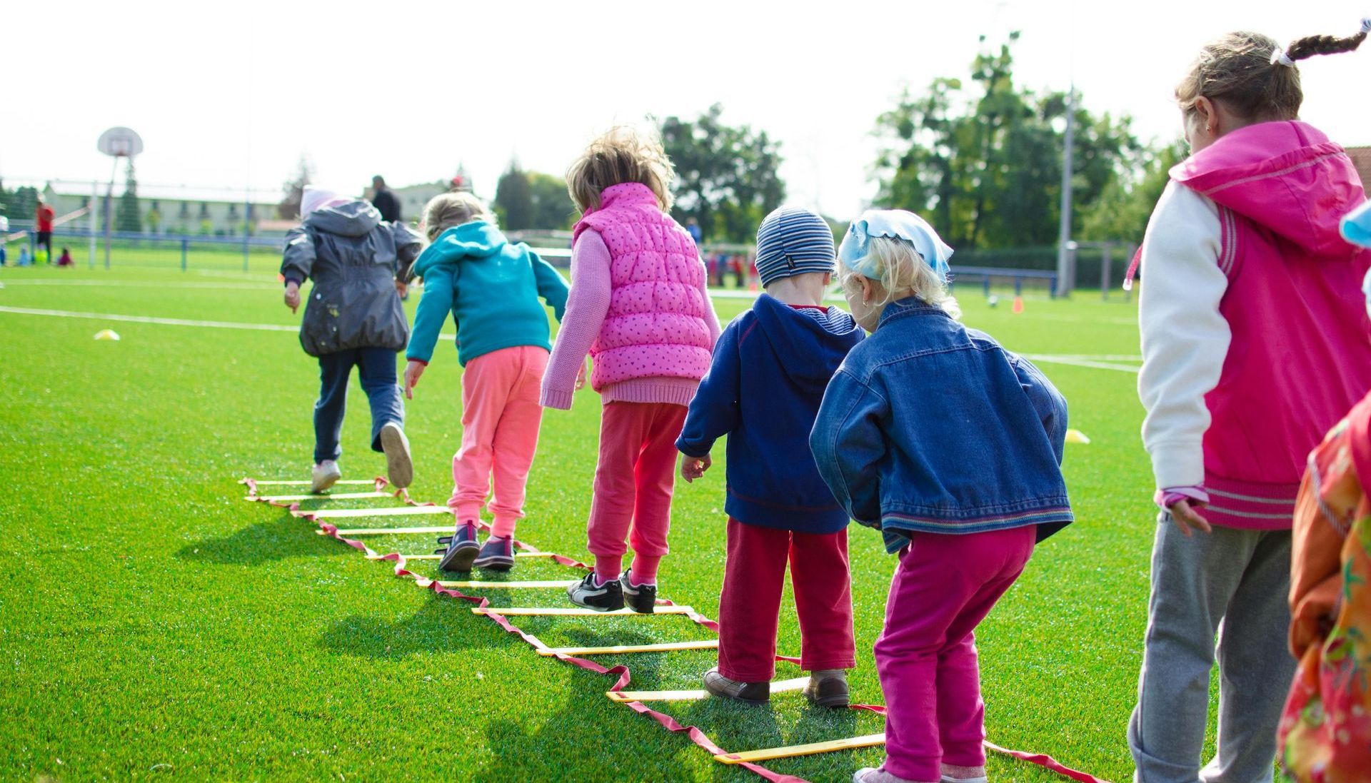 Children playing on an agility ladder on a green field.