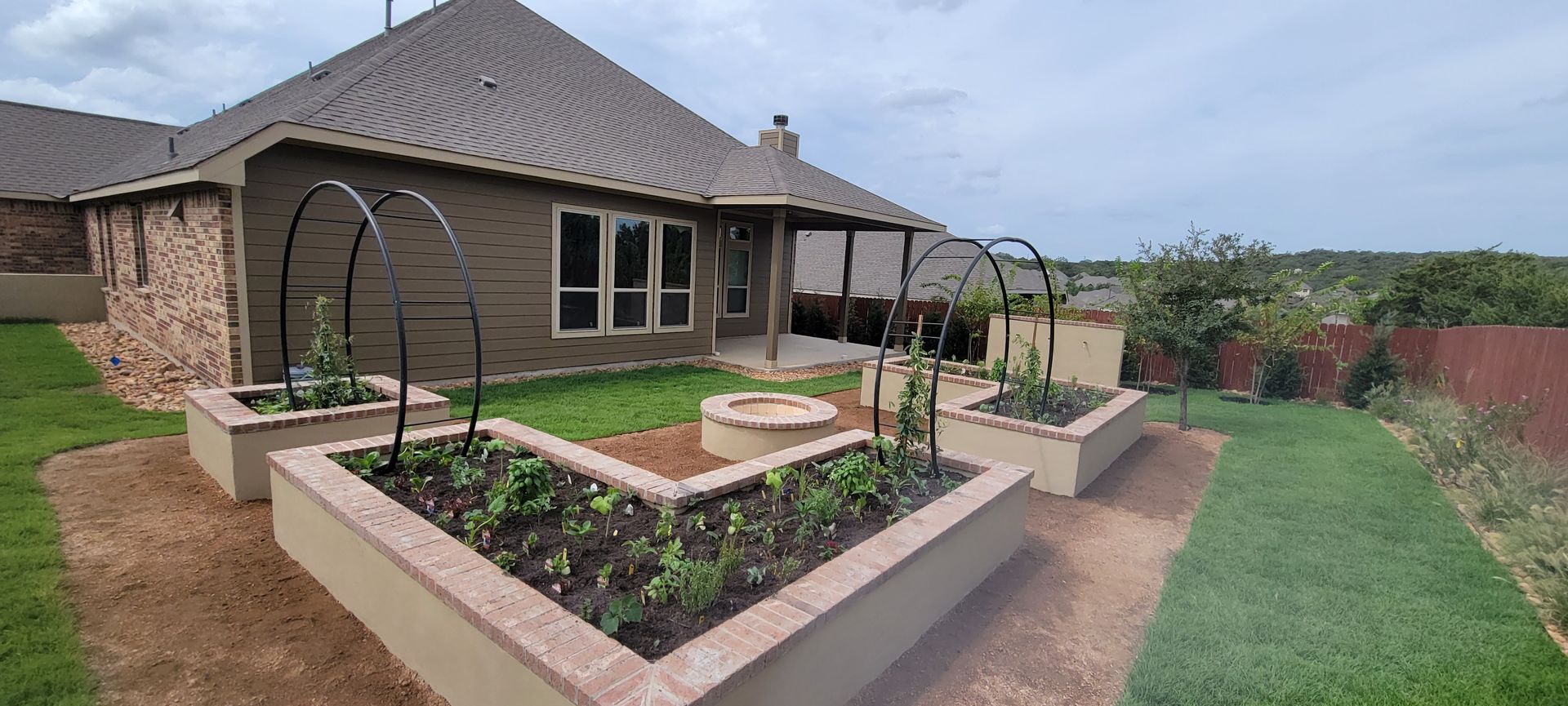 Outdoor water fountain built with brick and stucco, against a fence and trees, on a grassy lawn.