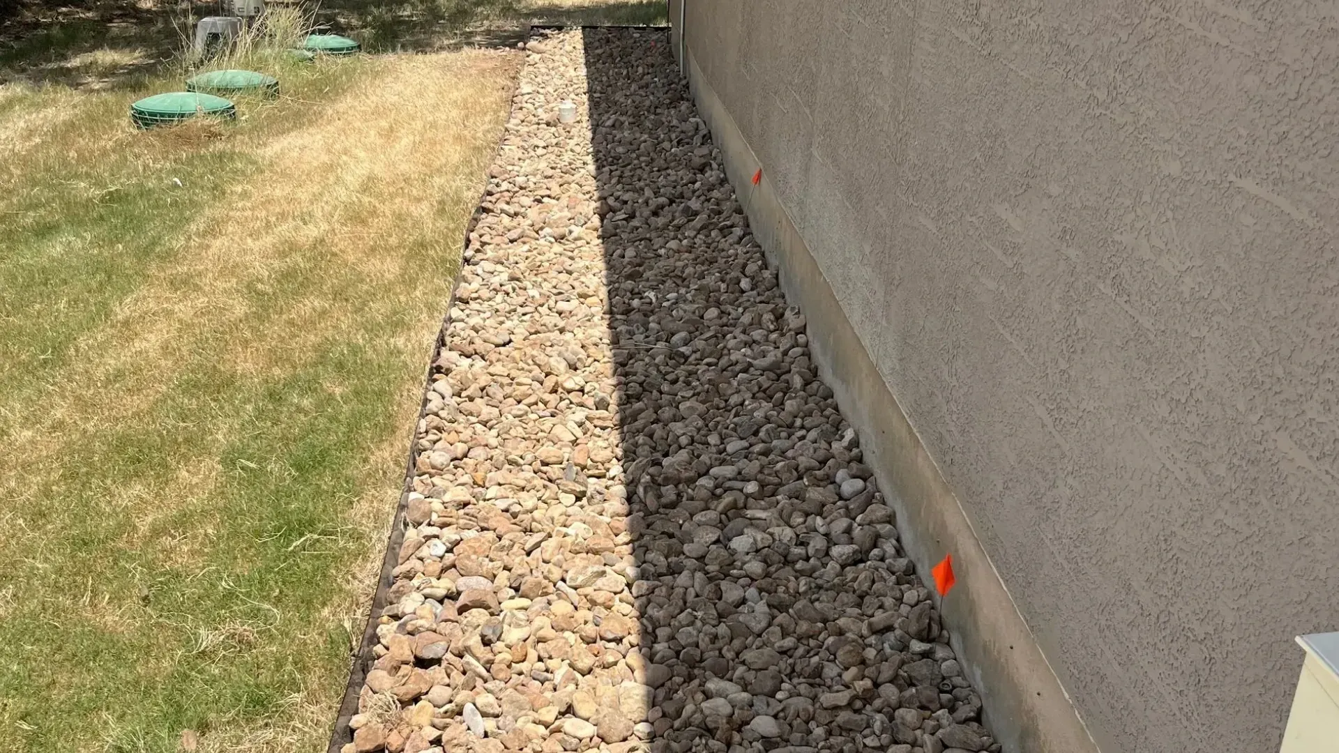 Gravel path alongside a beige stucco wall, next to a grassy lawn.
